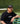 Man wearing black Mantis Snapback Cap and matching Mantis t-shirt sitting on bench at tennis court