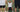 Man sitting on tennis court holding hands of two standing people, promoting Wimbledon tickets and tennis experience