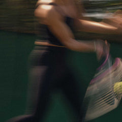 Blurred motion of a woman executing a forehand technique with a tennis racket and ball outdoors.