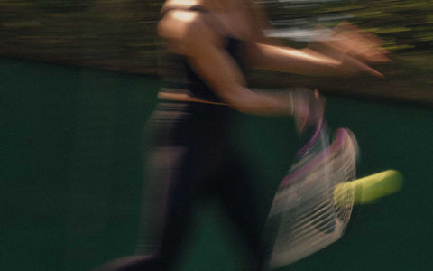 Blurred image of a tennis player dynamically swinging a racket to hit a ball demonstrating forehand technique