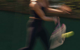 Blurred tennis player executing a forehand shot with racket and ball in motion on outdoor court, demonstrating forehand technique.