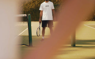man standing on tennis court holding racquet viewed through blurred arms demonstrating tennis lessons for beginners