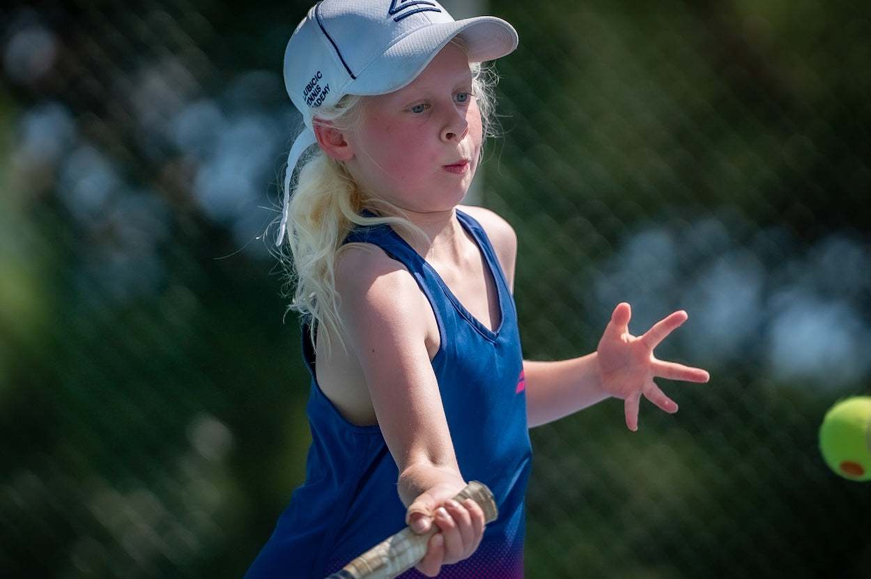 Young girl in blue sportswear playing tennis with a junior size tennis racket on an outdoor court