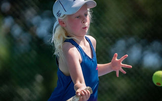 Young girl in blue sportswear playing tennis with a junior size tennis racket on an outdoor court