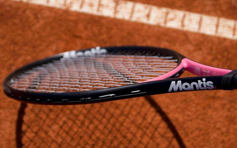 Close-up of a Mantis tennis racquet with black and pink frame and strings on a clay tennis court representing the best tennis strings for spin.