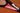 Close-up of a Mantis tennis racket frame showing US and UK flags and carbon fiber branding on a clay court background