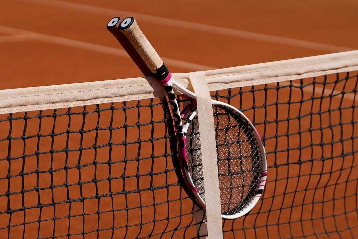 Two tennis racquets leaning against a net on a clay tennis court