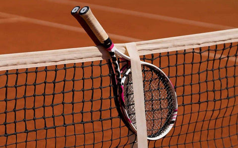 Two tennis racquets leaning against a net on a clay tennis court