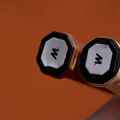 Close-up of two tennis racket handles with replacement grips and M logo end caps on brown background