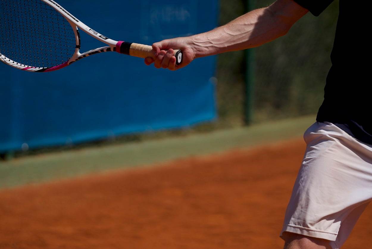 Tennis player gripping racket with forearm muscles visible, demonstrating prevention of tennis elbow through proper technique and equipment.