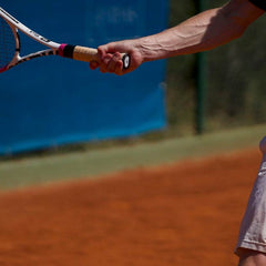 Tennis player gripping racket on clay court demonstrating forearm use to prevent tennis elbow