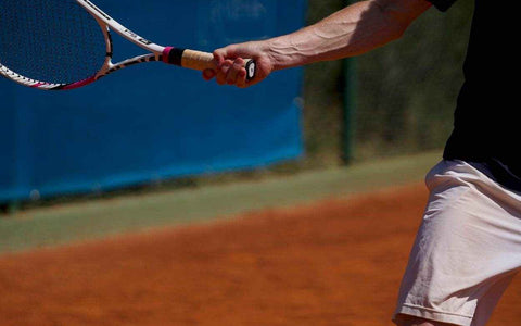 Tennis player gripping racket on clay court demonstrating how to prevent tennis elbow with proper technique
