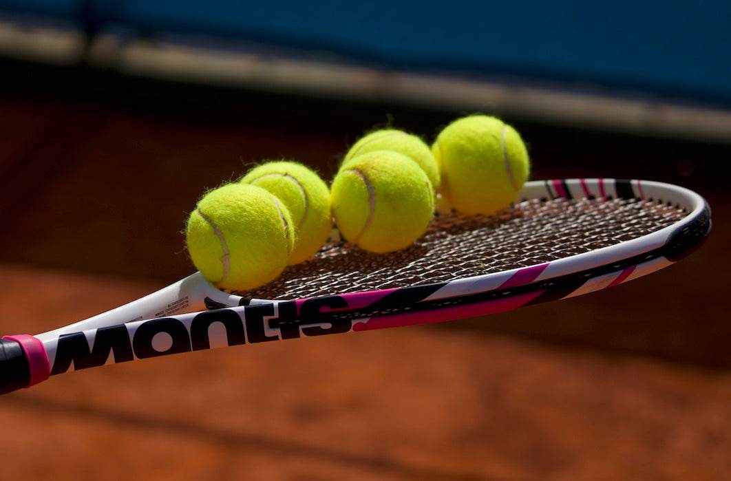 Tennis racket with five yellow tennis balls balanced on its strings on a clay court background