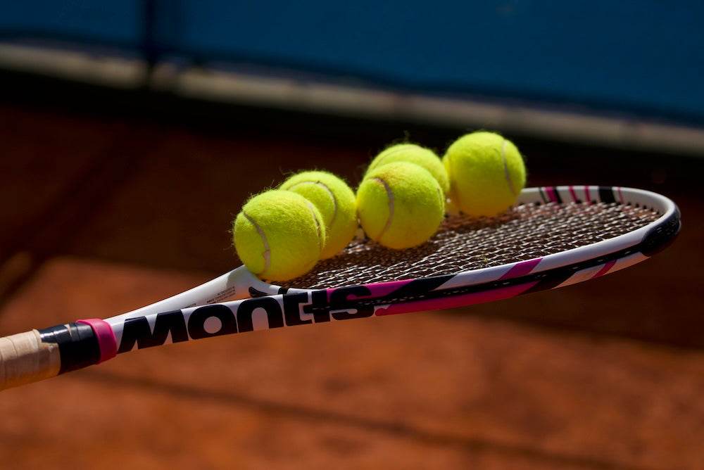 Close-up of a Mantis tennis racket with tennis balls on a clay court representing amateur tennis scene in the UK