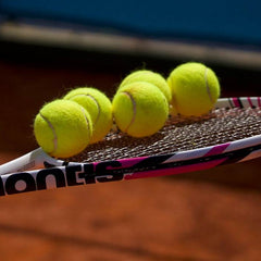 Tennis racket with five yellow tennis balls on clay court, illustrating how to compare tennis rackets for game performance.