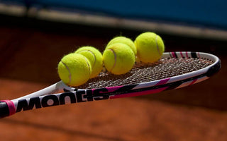 Tennis racket with multiple tennis balls balanced on the strings on a clay court background
