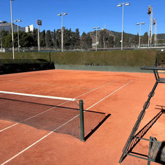 Empty clay tennis court with net and chair umpire stand under clear sky, ideal for tennis lessons for adults