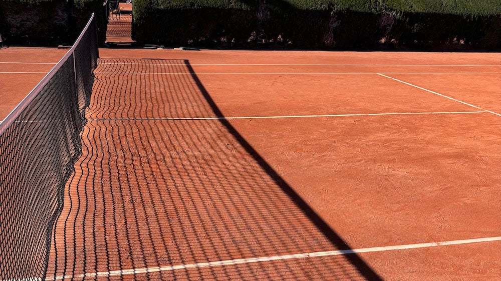 professional tennis coaching on an outdoor clay tennis court with net and shadows