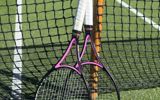 Two tennis racquets leaning against a net on a grass tennis court representing tennis racquet stringing tension concepts