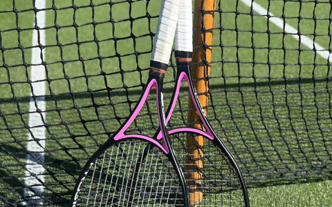 Two tennis racquets with white grips leaning against a net on a tennis court, illustrating tennis racquet stringing tension.