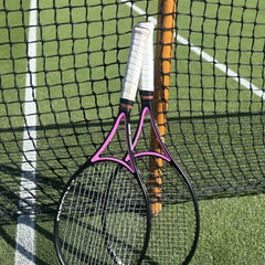 Two tennis racquets with white grips leaning against a net post on a grass tennis court symbolizing tennis racquet stringing tension.