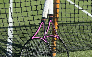 Two tennis racquets with white grips leaning against a net post on a grass tennis court, emphasizing tennis racquet stringing tension concepts.