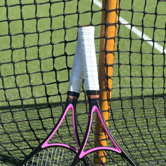 Two tennis rackets with white grips leaning against a net on a grass tennis court, illustrating the overgrip vs replacement grip comparison.