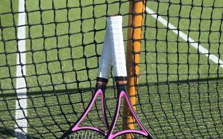 Two tennis rackets with white overgrips leaning against a net on a tennis court