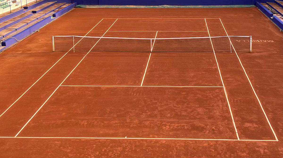 Clay tennis court with standard dimensions and white boundary lines including net in the center