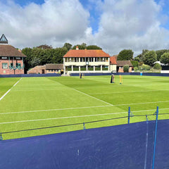 Grass tennis court with clear white boundary lines under a partly cloudy sky at a tennis club.