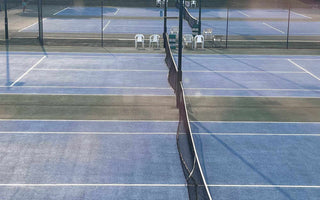 outdoor blue hard tennis court surface with nets and white markings under sunlight