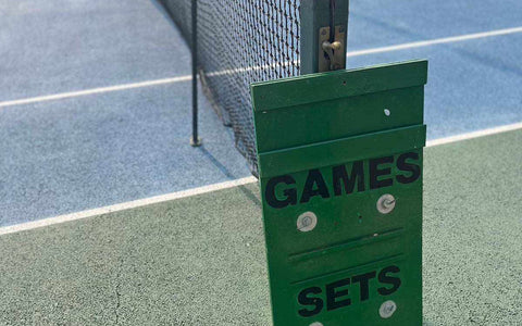 Tennis court with a net and green manual scoreboard showing games and sets, illustrating how to score in tennis