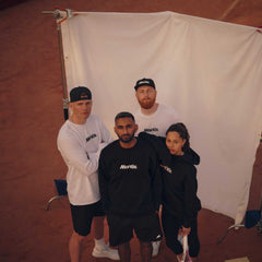 Group of diverse young adults wearing Mantis sportswear standing on a clay tennis court holding a tennis racket, promoting tennis for beginners.