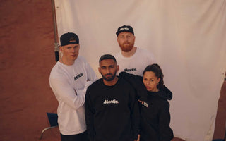 group of young adults in black and white mantis sportswear posing on a tennis court with a white backdrop, tennis for beginners clothing collection
