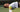 close-up of a tennis player lying on a hard court holding a bright yellow Mantis tennis ball labeled "all court" near the white boundary line