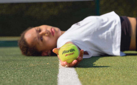 Tennis player lying on hard court holding a Mantis hard court tennis ball near the white line
