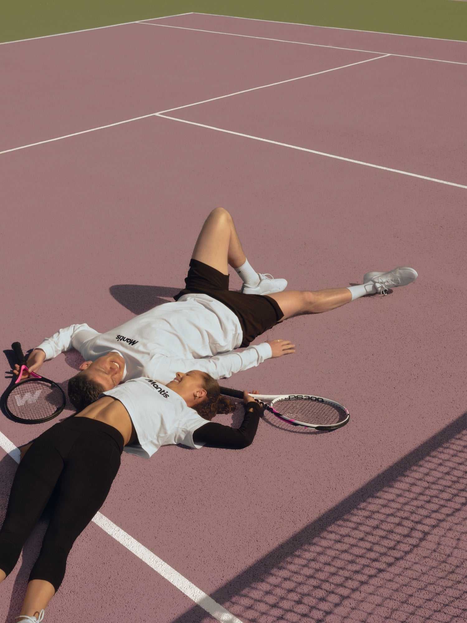 Mixed doubles tennis players resting on court with rackets on pink surface