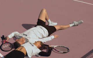 mixed doubles tennis partners lying on court with rackets on a sunny day