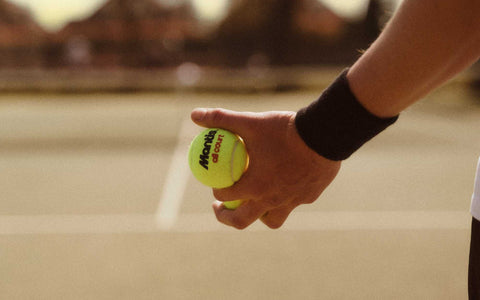 tennis player holding a bright yellow tennis ball on court for tennis volley drills practice