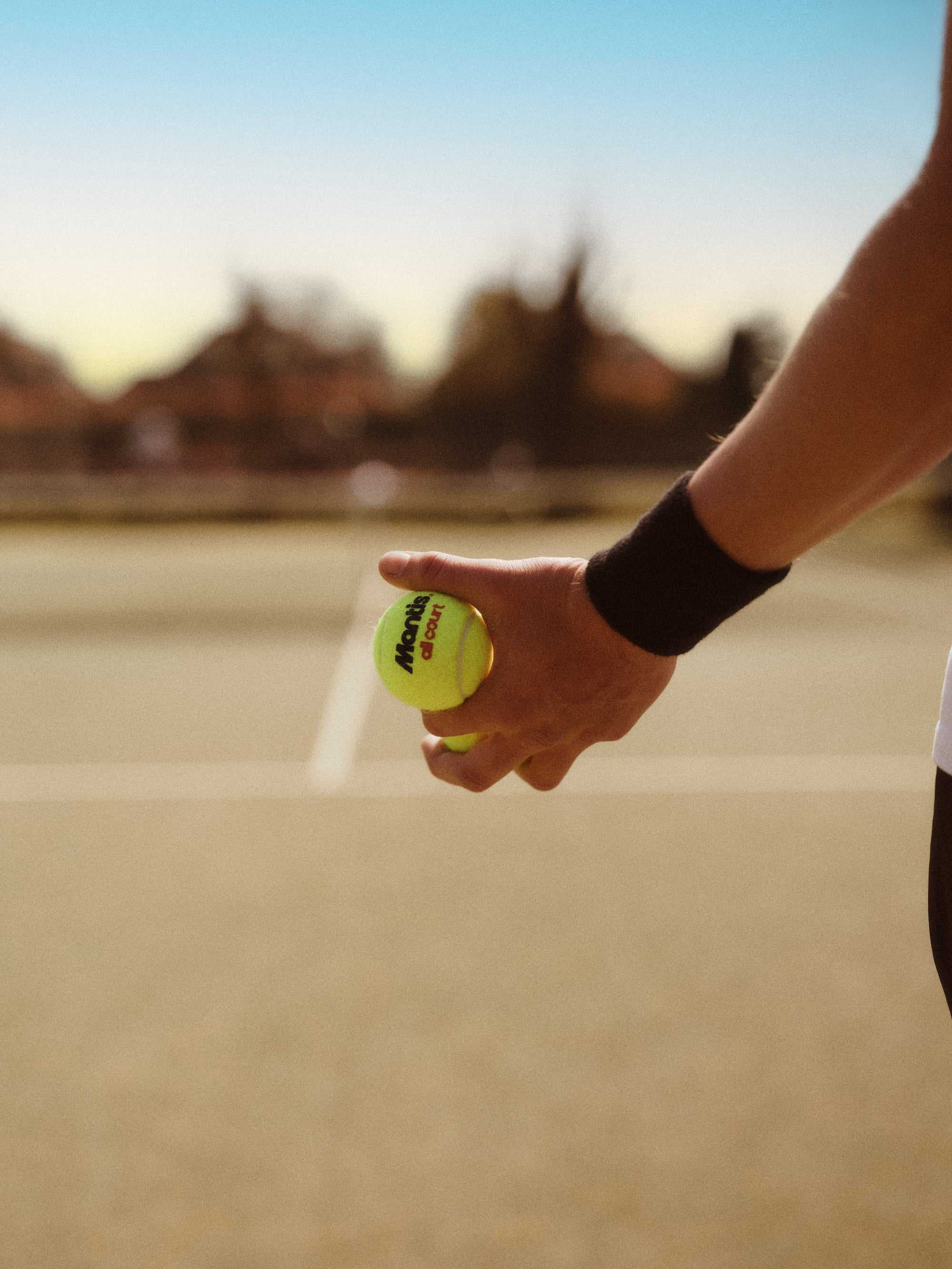 Tennis player holding a bright yellow Mantis tennis ball preparing to serve on an outdoor court at sunset, illustrating tennis volley drills practice.