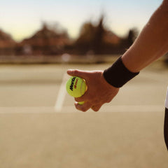 Tennis player holding a bright yellow Mantis tennis ball preparing to serve on an outdoor court at sunset, illustrating tennis volley drills practice.