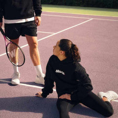 Two tennis players on court with one holding a Mantis racket, wearing branded sportswear, showcasing precision and craftsmanship.