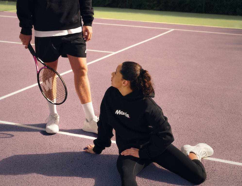 Two tennis players on court with one holding a Mantis racket and the other stretching, showcasing Mantis Rackets in use