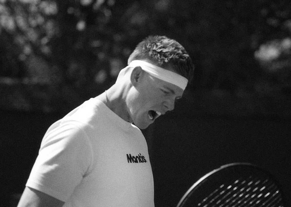 Black and white photo of a tennis player wearing a Mantis shirt and headband showing intense focus and mental toughness on court