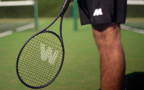Person holding a tennis racket on a tennis court, ready to play after restringing.