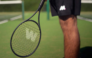 Tennis player holding a black tennis racket ready on a grass court, illustrating restring a tennis racket guide.