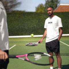 Two men playing tennis on a green court with one preparing to hit a ball using a pink and black tennis racket, showcasing best tennis rackets for spin.