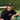 Man wearing black Mantis Snapback Cap and matching Mantis t-shirt sitting on bench at tennis court