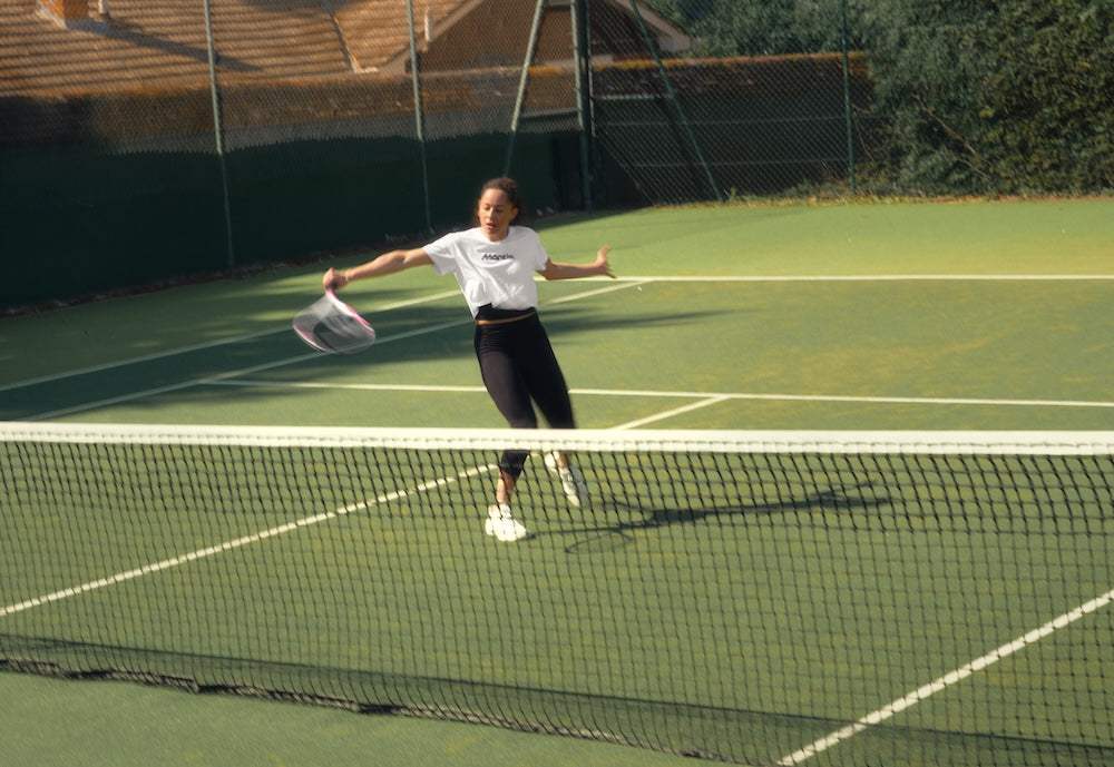 female tennis player swinging racket on outdoor tennis court during daytime
