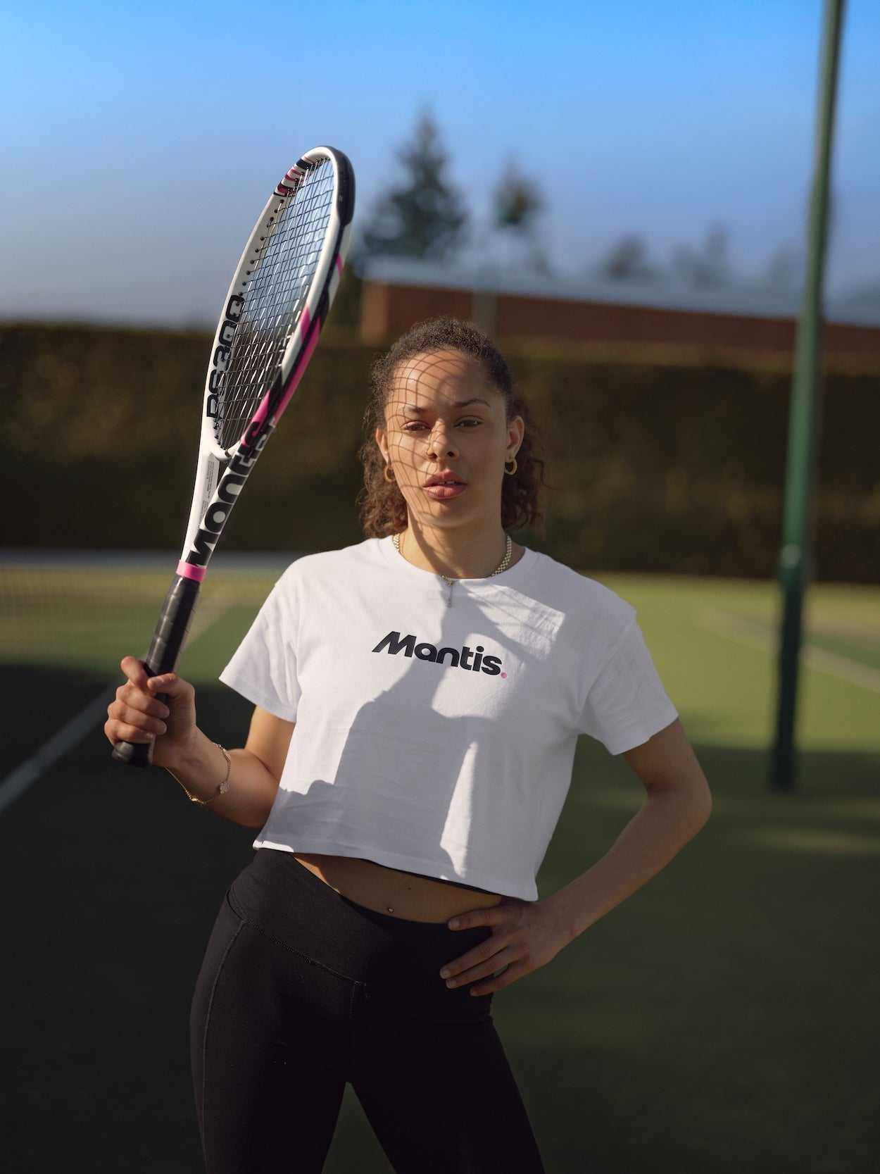 Woman holding tennis racket on outdoor court wearing Mantis shirt for buying a tennis racket guide